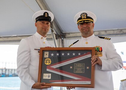 NORFOLK, Va. (Sept. 22, 2022) Cmdr. Gregory J. Piorun, Jr., commanding officer of the Ticonderoga-class, guided-missile cruiser USS Anzio (CG 68), right, receives a cased ensign from Command Master Chief Dallas G. Roberts, left, during the ship’s decommissioning ceremony onboard Naval Station Norfolk, Sept. 22, 2022. Anzio was decommissioned after 30 years of service.  (U.S. Navy photo by Mass Communication Specialist 3rd Class Bradley Rickard)