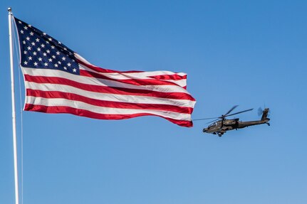 An Apache helicopter flies by an American flag