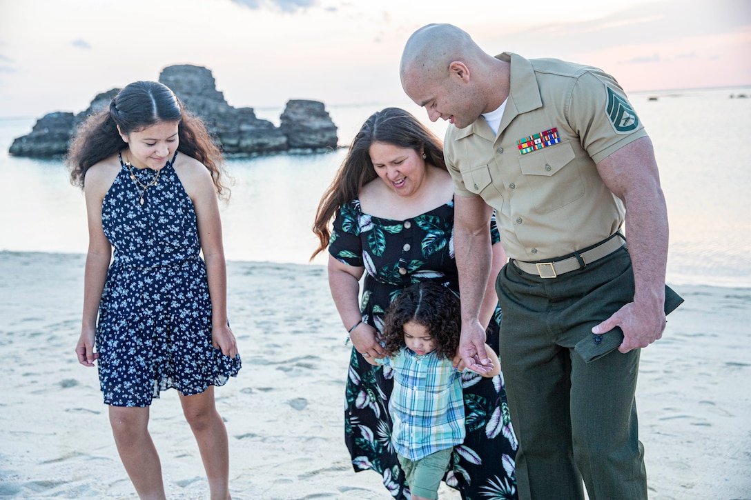 A uniformed service member, a woman and two children walk near a beach.