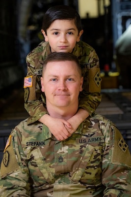 A small boy in a uniform stands behind a man in uniform.