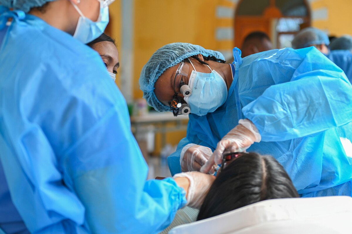 A group of service members in medical gear perform dental work.