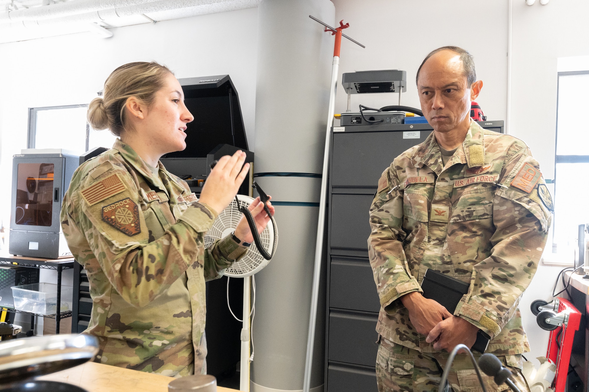 Staff Sgt. Carli Meis, left, 436th Airlift Wing Bedrock Innovation Lab intern, shows Col. Rudolph Cachuela, Air Mobility Command surgeon general, a radio communication device that was conceptualized at the Bedrock Innovation Lab, Dover Air Force Base, Delaware, Sept. 20, 2022. Cachuela also toured the 436th Medical Group and Air Force Mortuary Affairs Operations. (U.S. Air Force photo by Mauricio Campino)