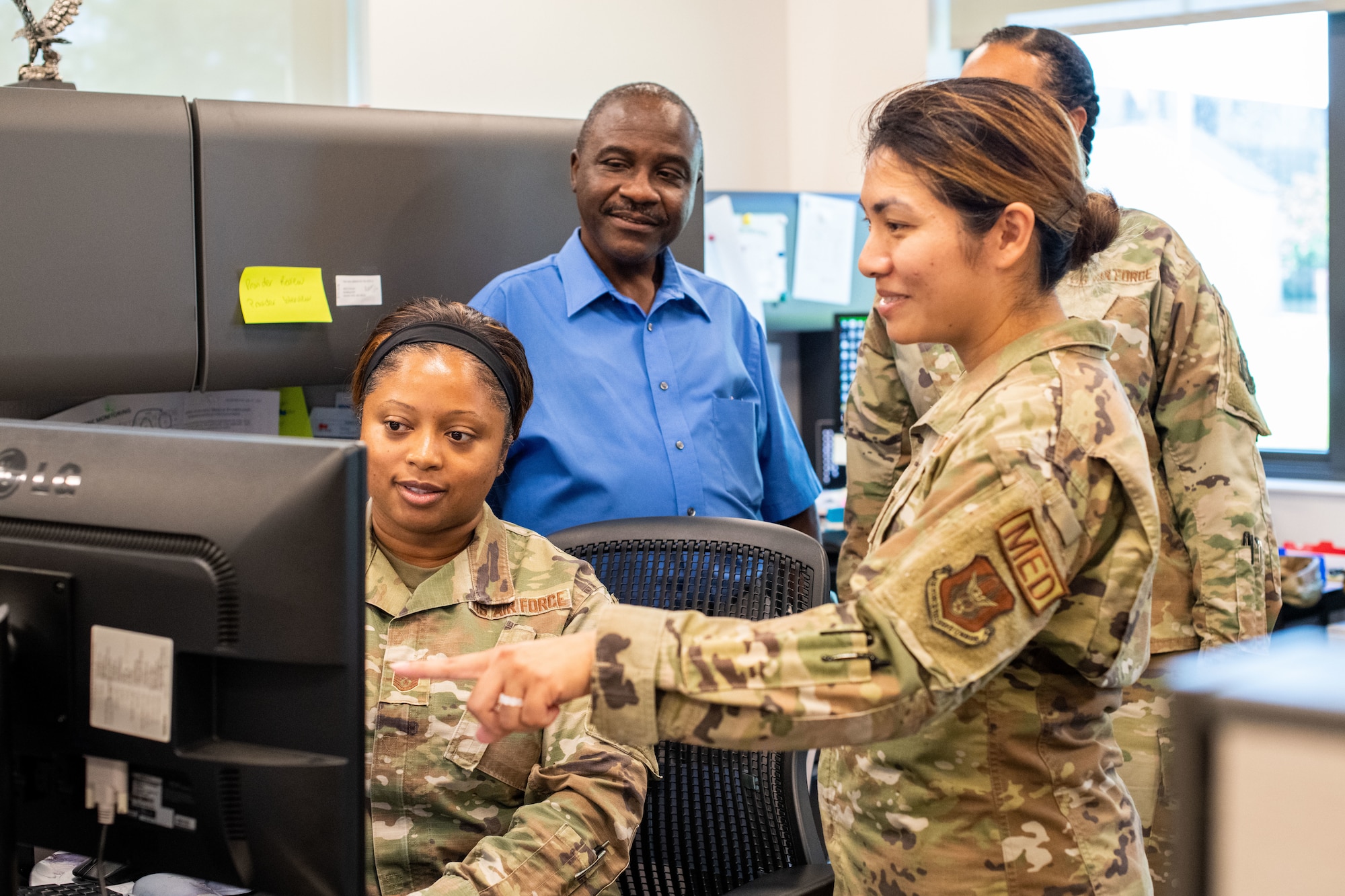 One Airman sits at a computer while three others stand around her