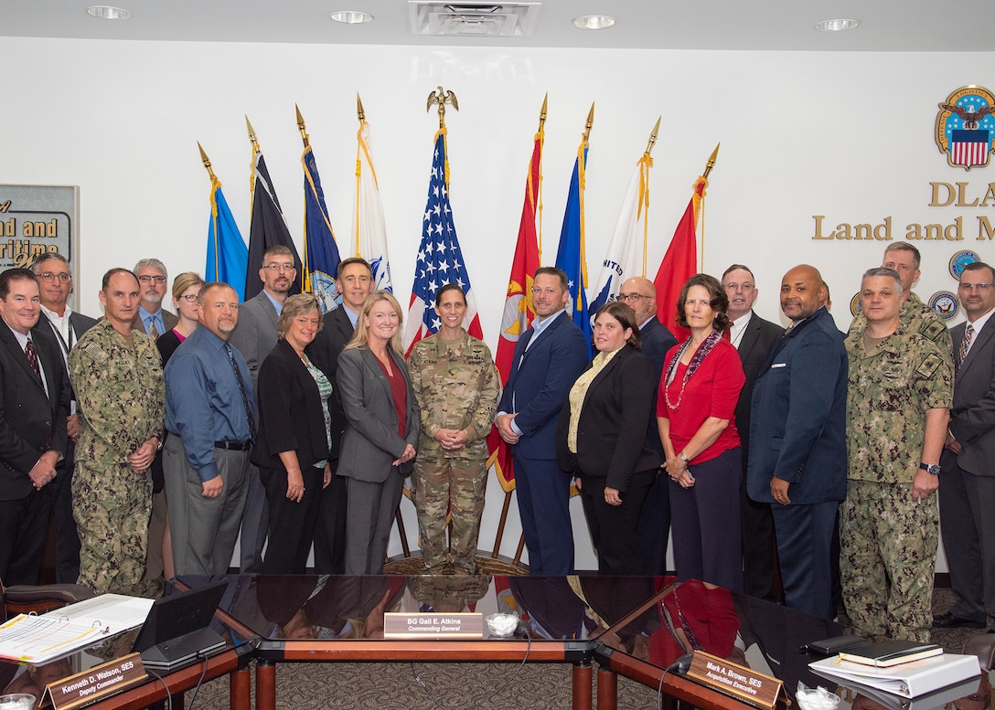 A large group of people both in uniform and out of uniform in a conference room in front of nine flags.