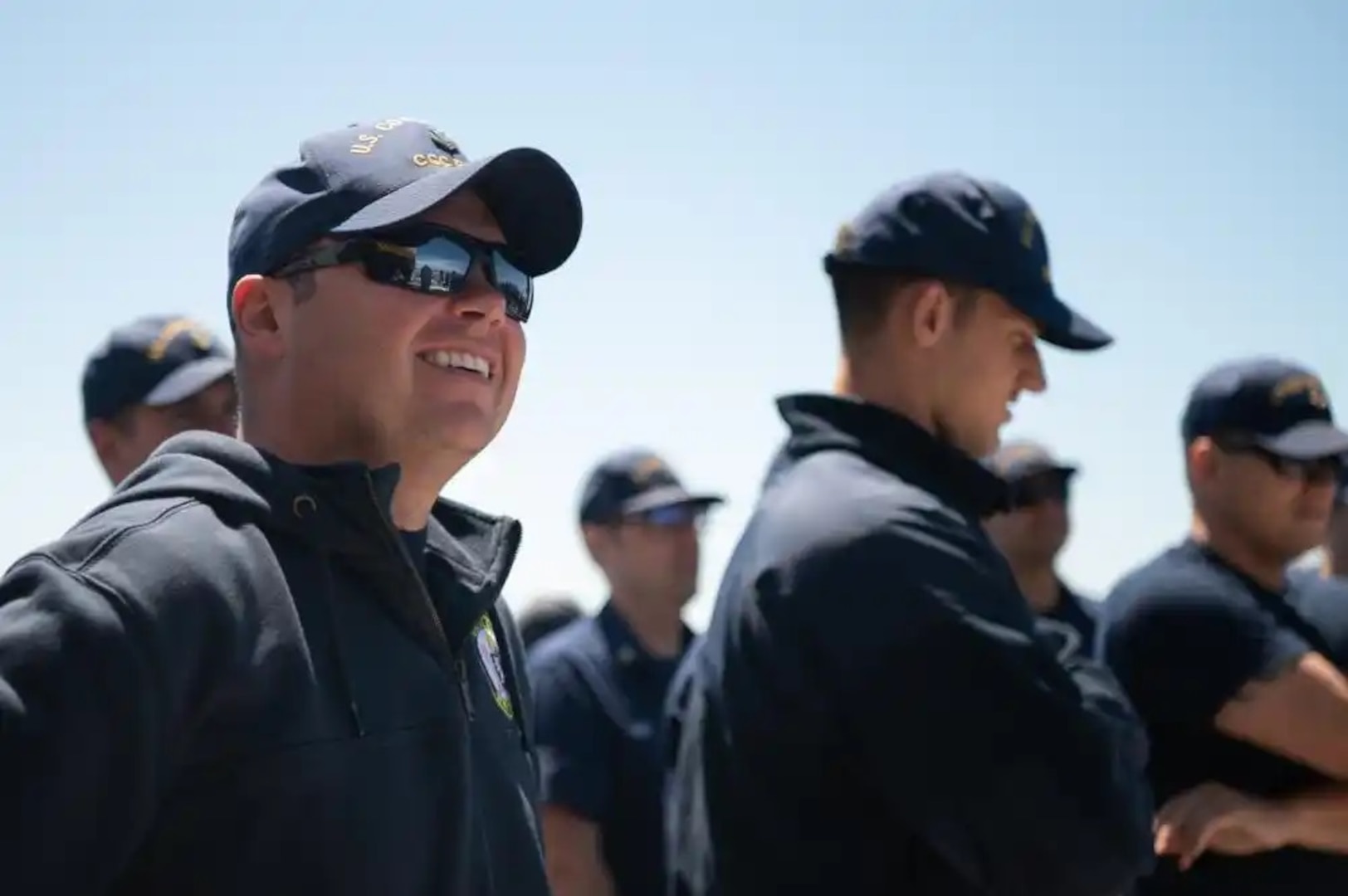 U.S. Coast Guard Petty Officer 1st Class Kristopher Gordon, an operations specialist aboard Coast Guard Cutter Bear, smiles as he pays attention to the command brief at quarters, Atlantic Ocean, July 27, 2022. The Bear and its crew are deploying to support the Northern Atlantic Fisheries Organization, deter illegal fishing and increase maritime domain awareness in tandem with its partner nations. (U.S. Coast Guard photo by Petty Officer 3rd Class Matthew Abban)