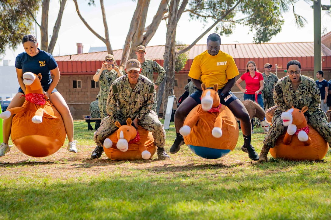 Four sailors ride on stuffed animals as others watch.