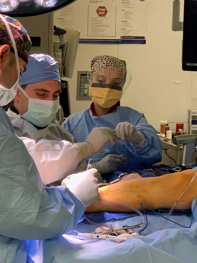 Three people in surgical gowns, masks and head coverings in a surgical suite.