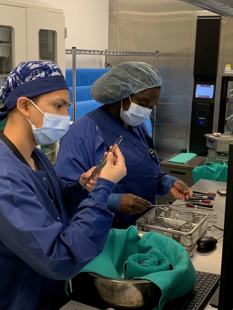 Two people in blue scrubs with head coverings holding surgical instruments.