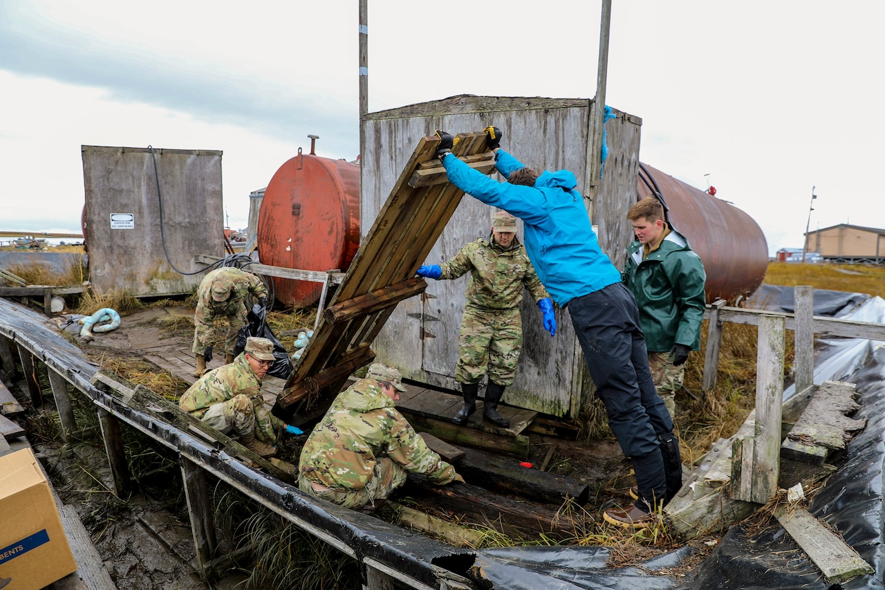 National Guardsmen lift wood debris at an outdoor site.