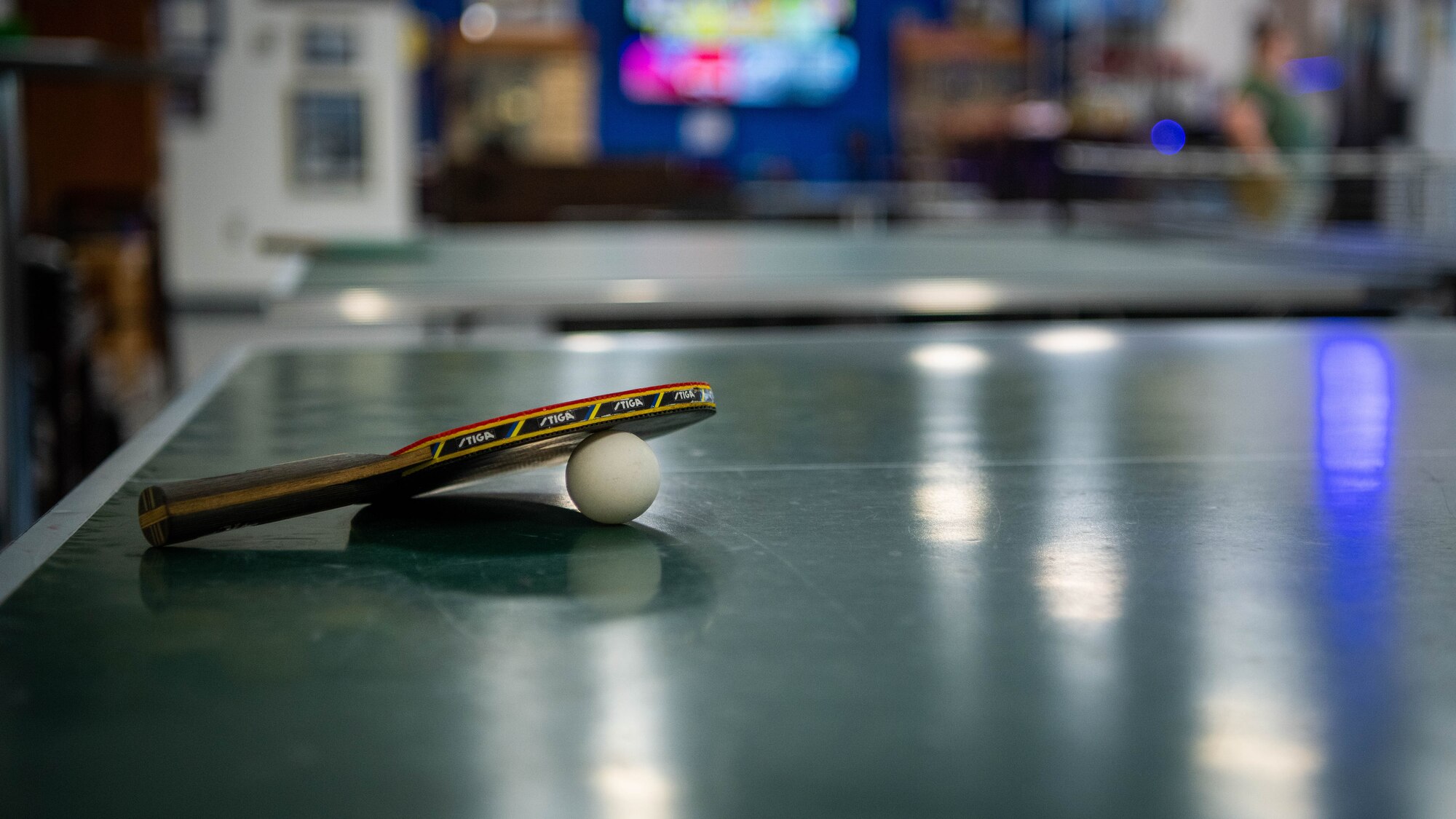 Table tennis paddle and ball sits on table.