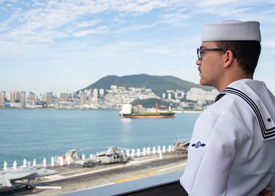 BUSAN, Republic of Korea (Sept. 23, 2022) Airman Sean Farrell, from Camarillo, California, mans the rails as the U.S. Navy’s only forward-deployed aircraft carrier, USS Ronald Reagan (CVN 76), pulls in to Busan, Republic of Korea, for a routine port visit. Ronald Reagan, the flagship of Carrier Strike Group 5, provides a combat-ready force that protects and defends the United States, and supports alliances, partnerships and collective maritime interests in the Indo-Pacific region. (U.S. Navy photo by Mass Communication Specialist 3rd Gorge Cardenas)