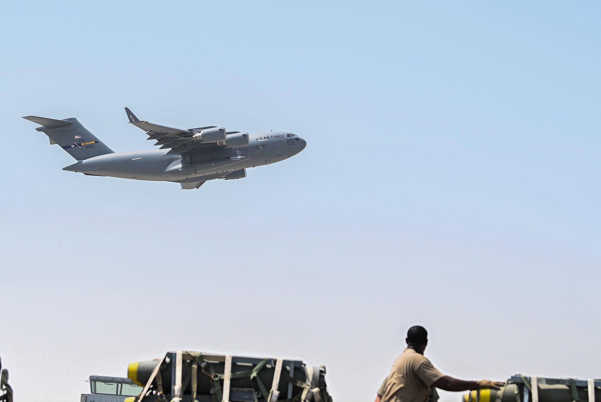 Airmen from the 379th Expeditionary Logistics Readiness Squadron transport munitions as a C-17 Globemaster III aircraft flies by Sept. 20, 2022 at Al Udeid Air Base, Qatar. The 379th ERLS ground transport team moved munitions from the munitions storage area to a staging area where they were later loaded onto a C-17. (U.S. Air National Guard photo by Master Sgt. Michael J. Kelly)