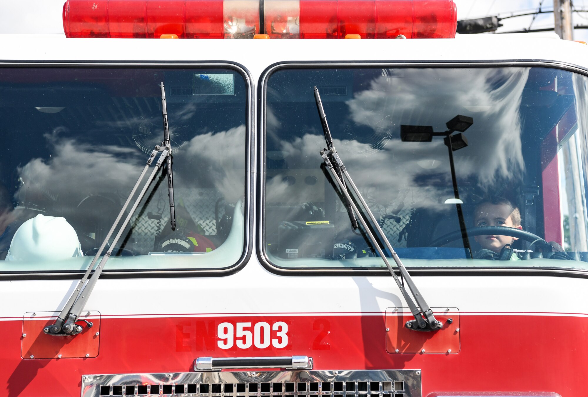 Young boy sits in driver seat of a fire truck, seen through windshield