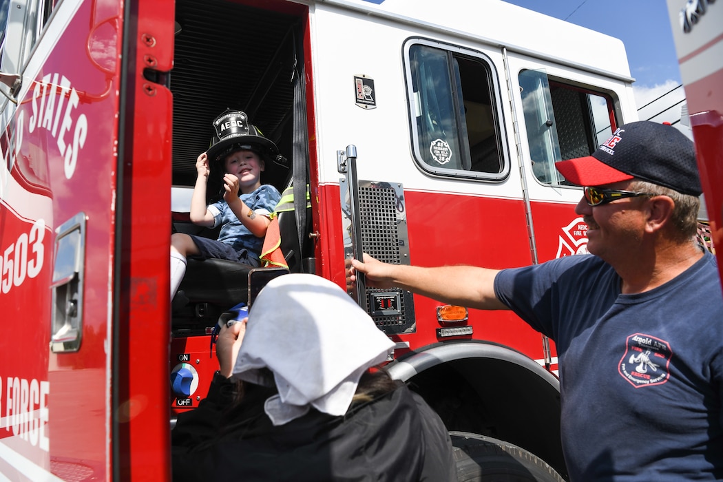 Young boy tries on firefighter helmet as a firefighter and his mother watch