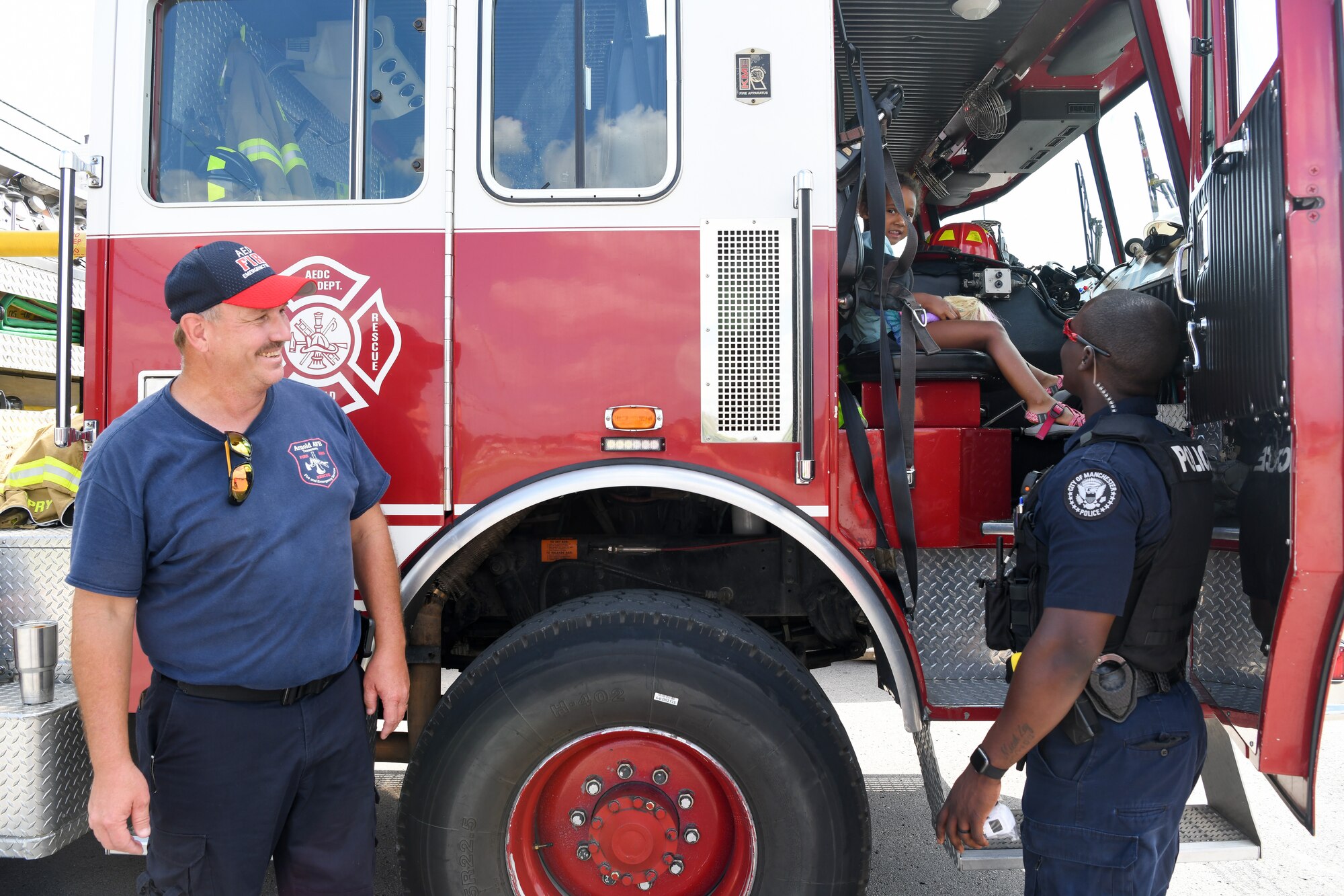 Police officer looks at daughter sitting in fire truck as firefighter looks on