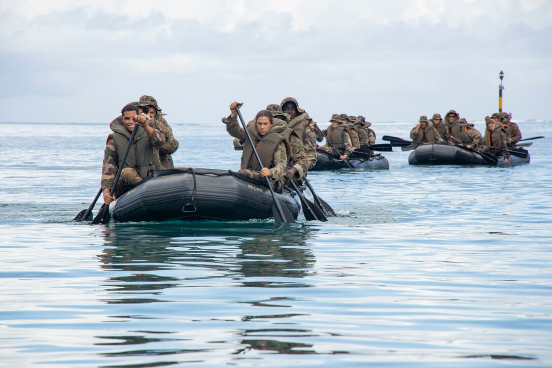 Marines paddle rubber rafts through the water.