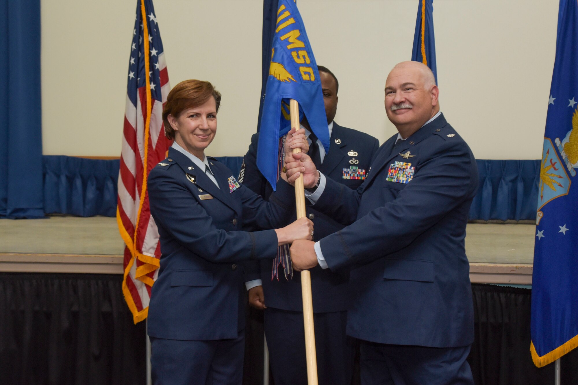 eoman in dress Air Force blues takes a unit flag from a man in Air Force dress blues.