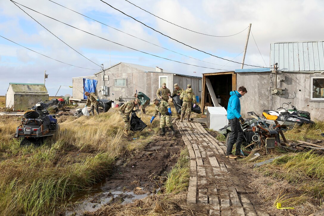 Service members clean up debris along a damaged boardwalk near buildings.