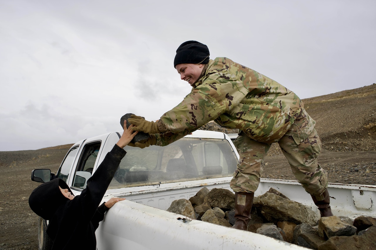A child hands a rock to a service member standing in the back of a pickup truck.