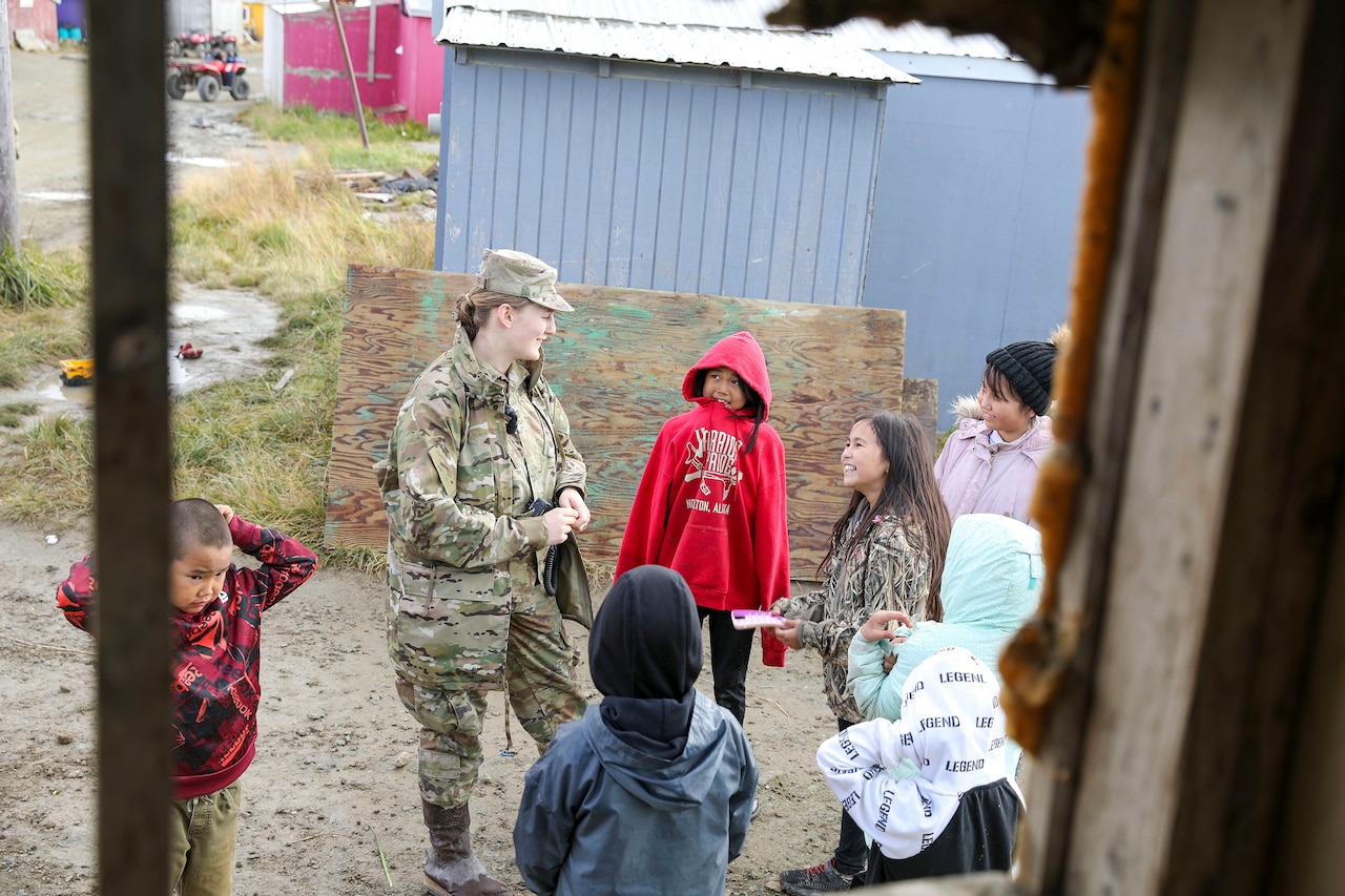 A service member talks to a group of civilians outside a building.