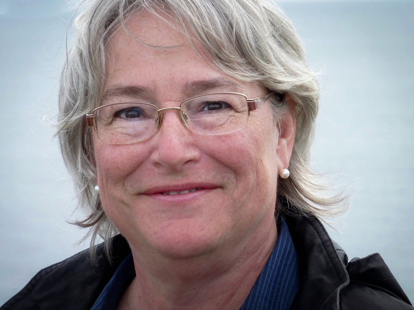 a photo of a grey haired woman in wire rimmed glasses smiling at the camera
