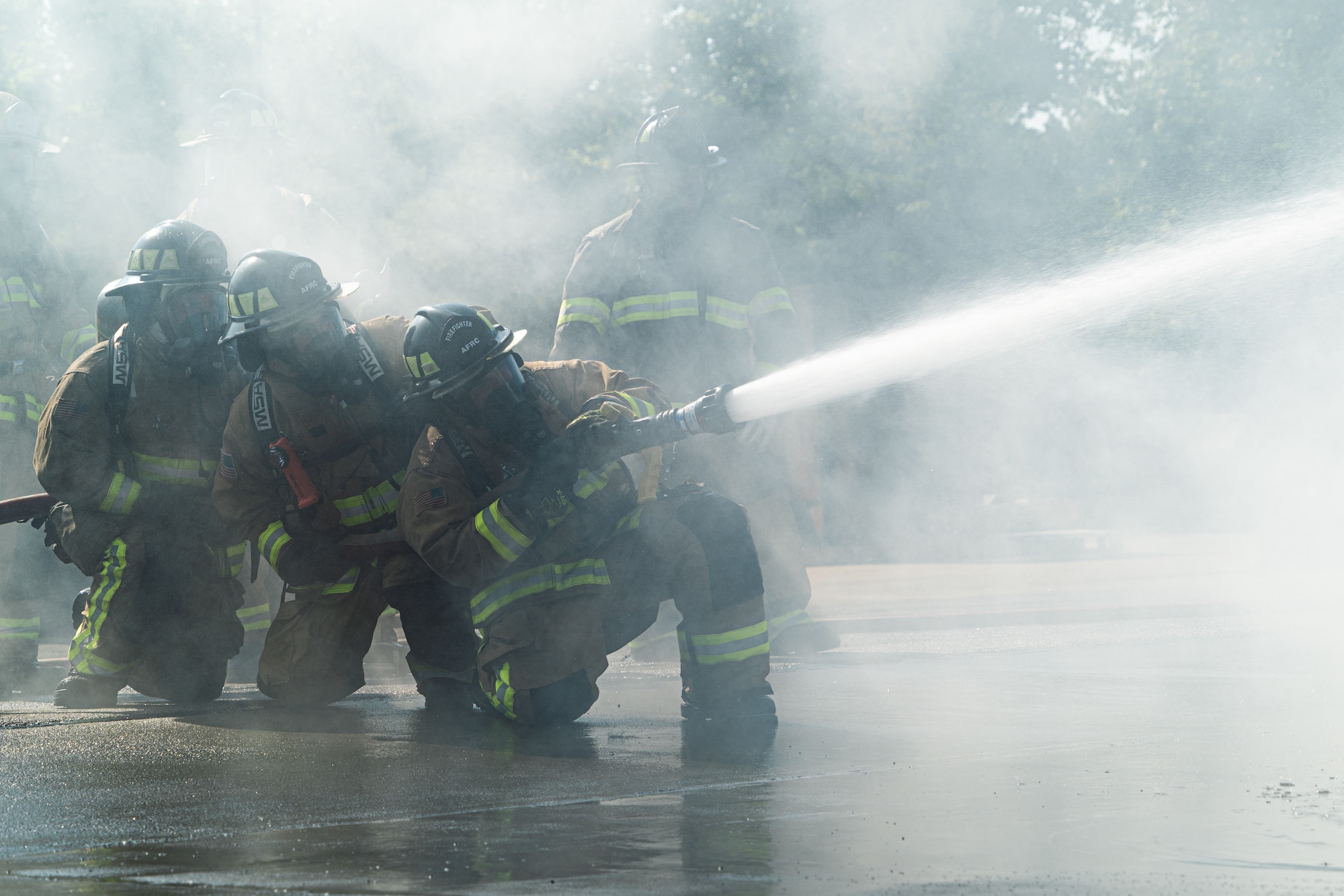 Firefighters with the 914th Fire Emergency Services kneel within a cloud of smoke while attempting to put out a simulated aircraft's fire during training.