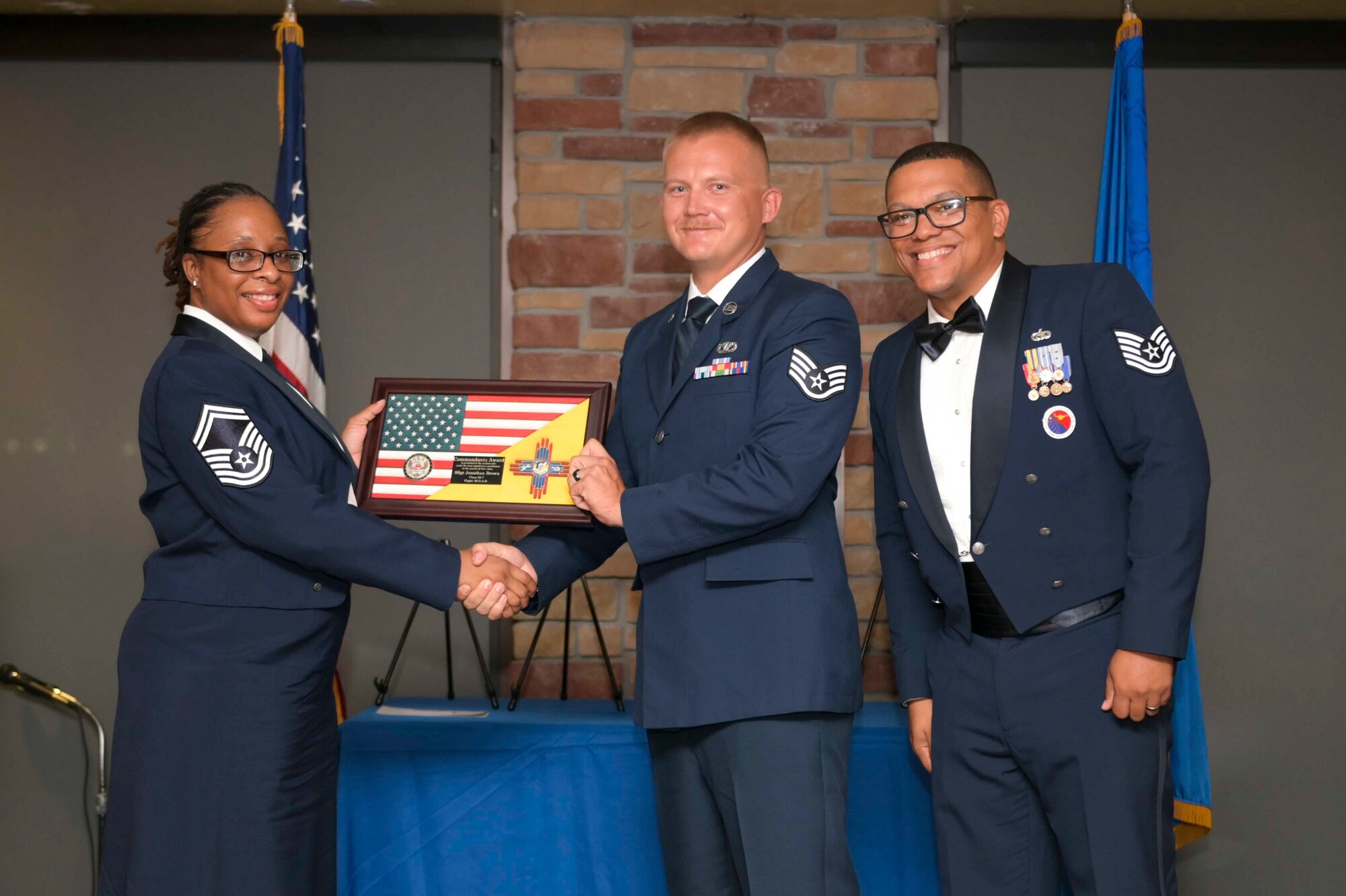 U.S. Air Force Staff Sgt. Jonathan Brown, center, accepts the Commandant's Award from U.S. Air Force Senior Master Sgt. Daisha Brown, 49th Logistics Readiness Squadron material maintenance superintendent, left, and Holloman Airman Leadership School Commandant U.S. Air Force Tech. Sgt. Briton Hurdle during an ALS graduation at Holloman Air Force Base, New Mexico, Sept. 22, 2022. The commandant leadership award is selected by the ALS commandant and is presented to the student who demonstrates the characteristics of an effective leader. (U.S. Air Force photo by Tech. Sgt. Victor J. Caputo)