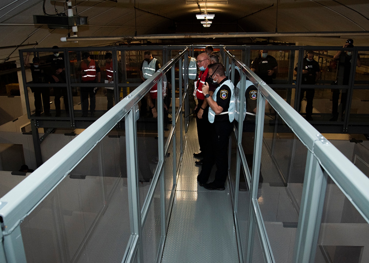 People in reflective gear and uniforms with radios stand on a observation catwalk at the DSCC Shoot House in Building  18.