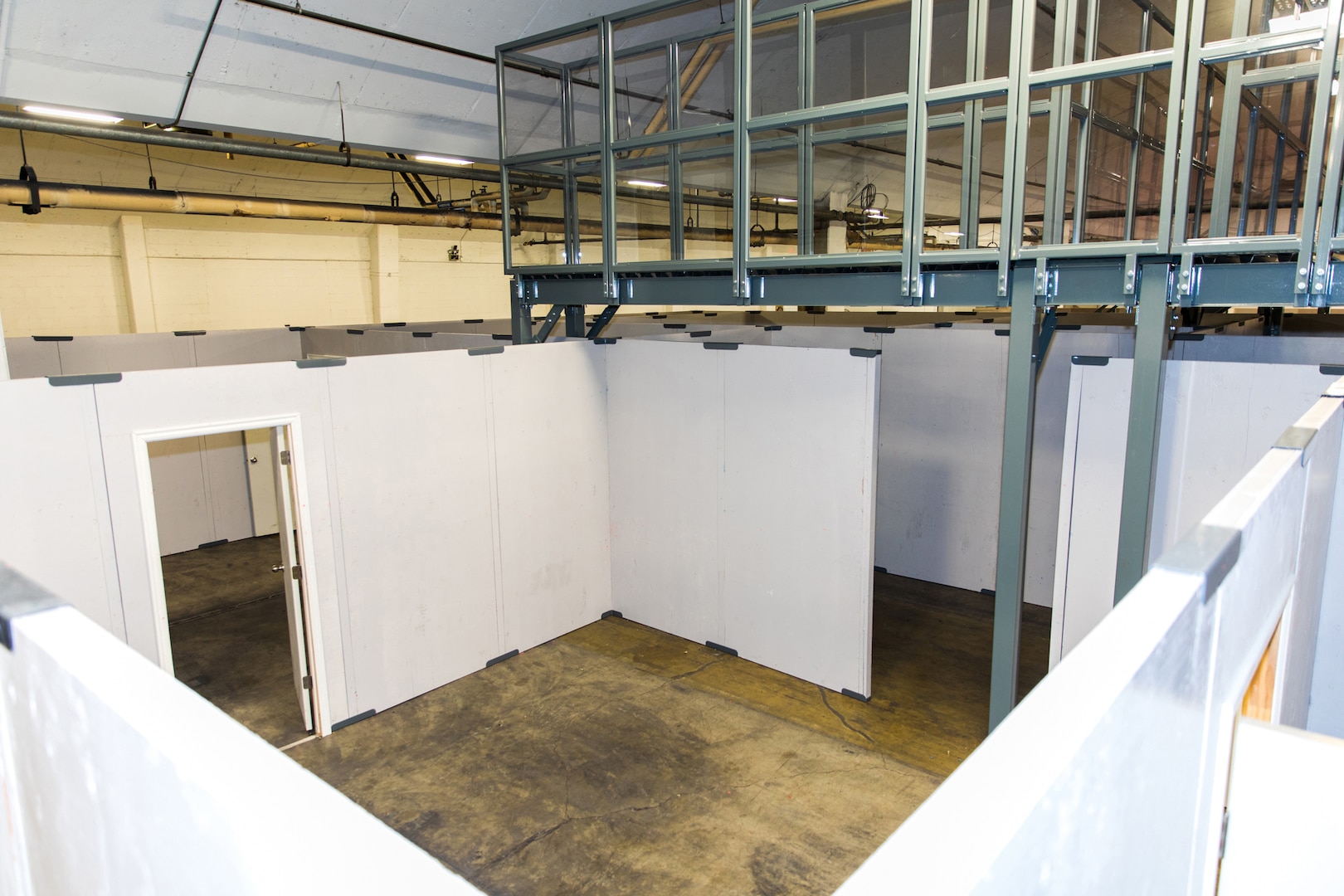 A photo of the inside of a shoot house. White walls, cement floor and a silver catwalk at the top for observation.