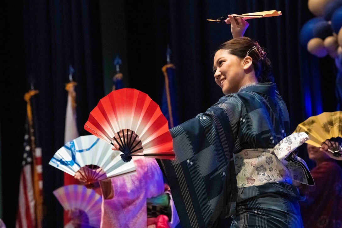 A woman performs a dance with others using paper fans.