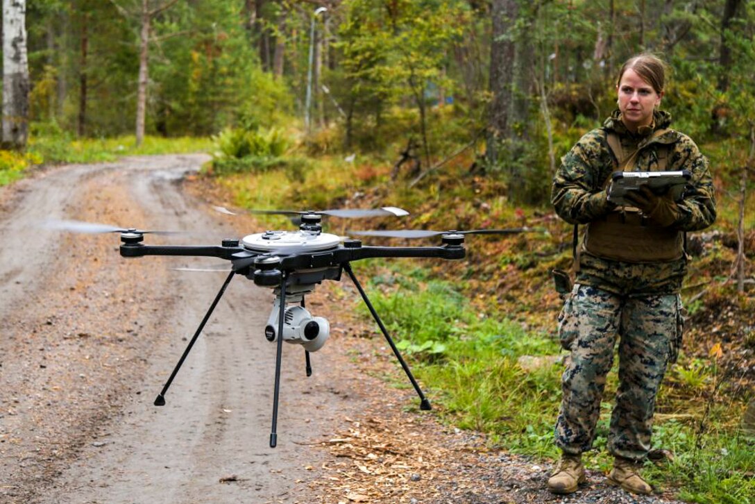 A Marine launches an unmanned aerial system along a dirt road in a wooded area.