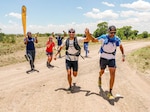 Airman crosses finish line holding hands with competitor.