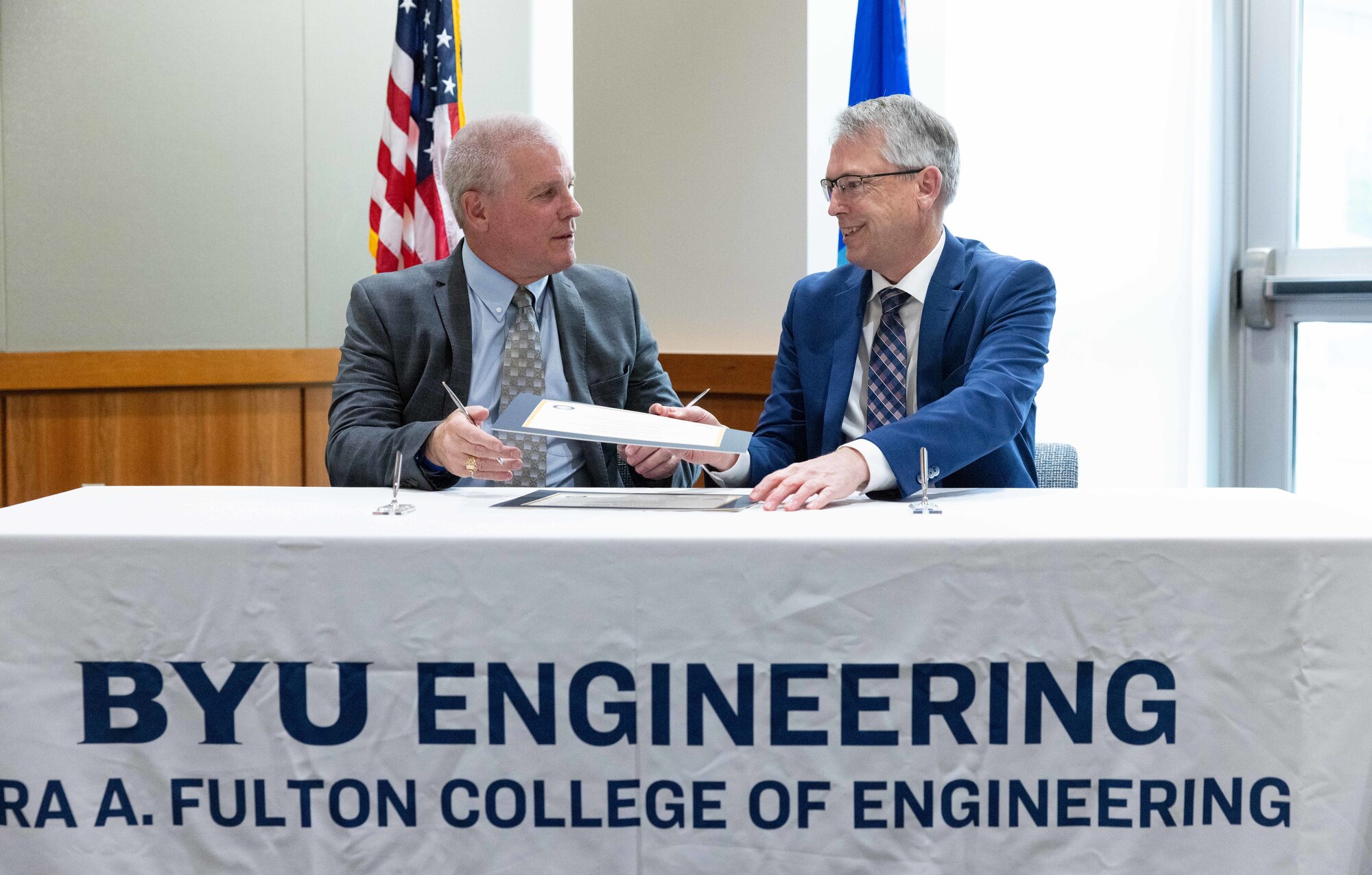 Two men sit at a table signing an agreement.