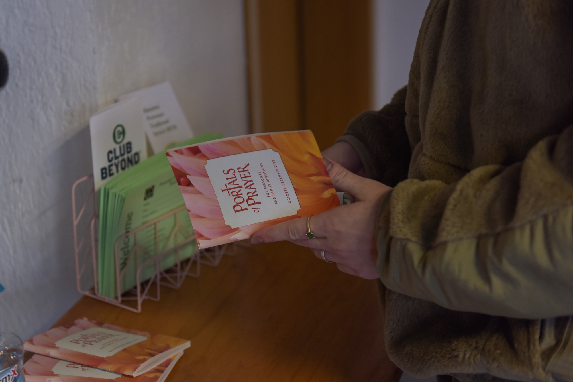 A woman opens an orange devotional pamphlet titled 'Portals of Prayer'