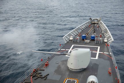 A large gun fires on the deck of a ship.