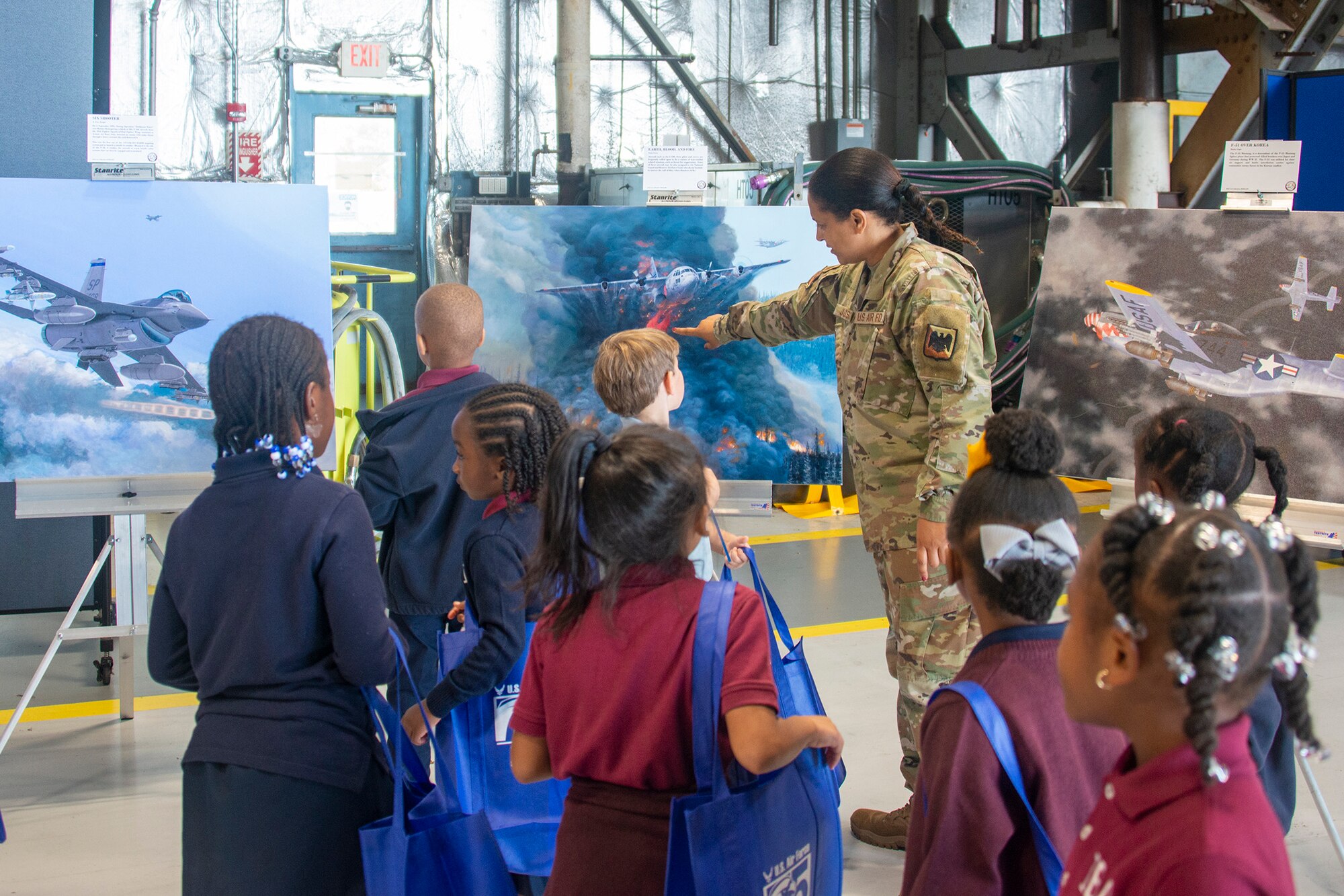 A chaperone talks about the Department of the Air Force Art Program artwork on display to students at a science, technology, engineering, arts and mathematics exhibit at the Joint Base Andrews 2022 Air and Space Expo Sept. 16, 2022.