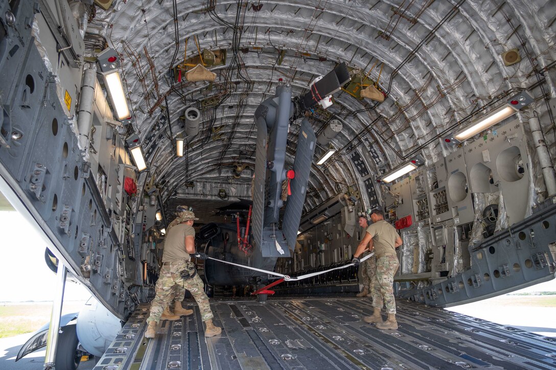 Airmen move a helicopter inside an open aircraft.