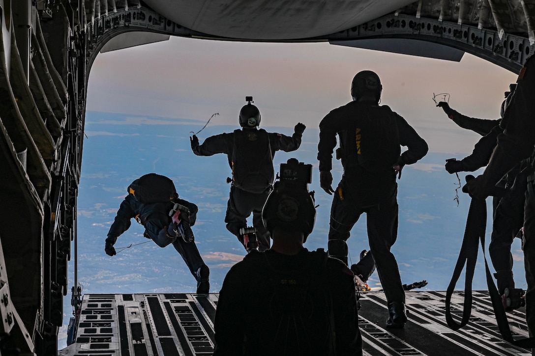 Service members jump out of an airborne aircraft.