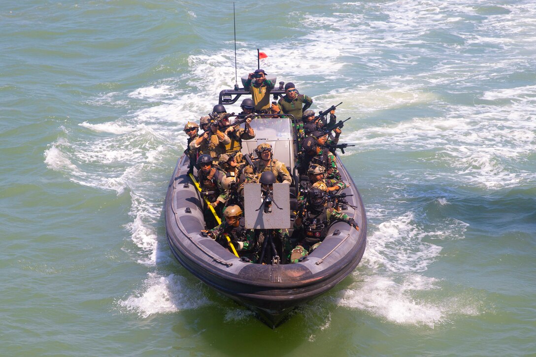 U.S. and Indonesian troops in a small rubber boat aim weapons.