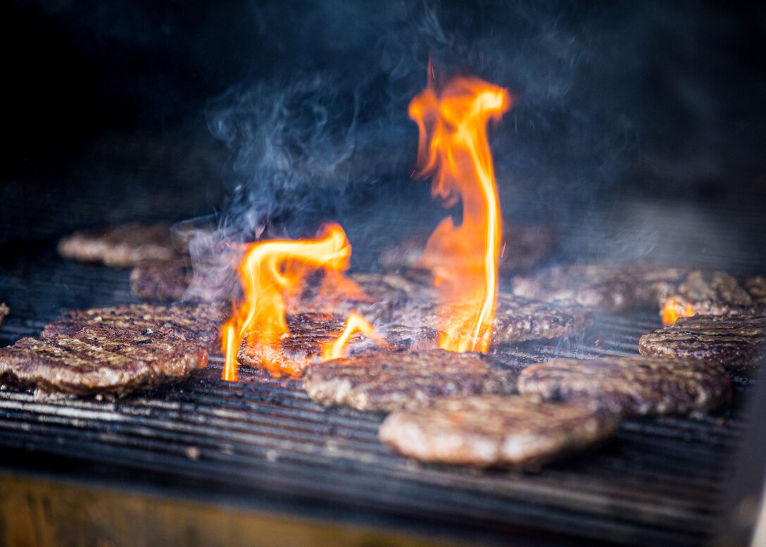 hamburgers sizzling with fire on a grill.
