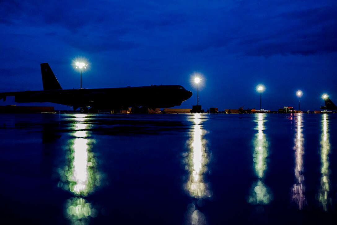 A large aircraft sits on a tarmac on a rainy night.