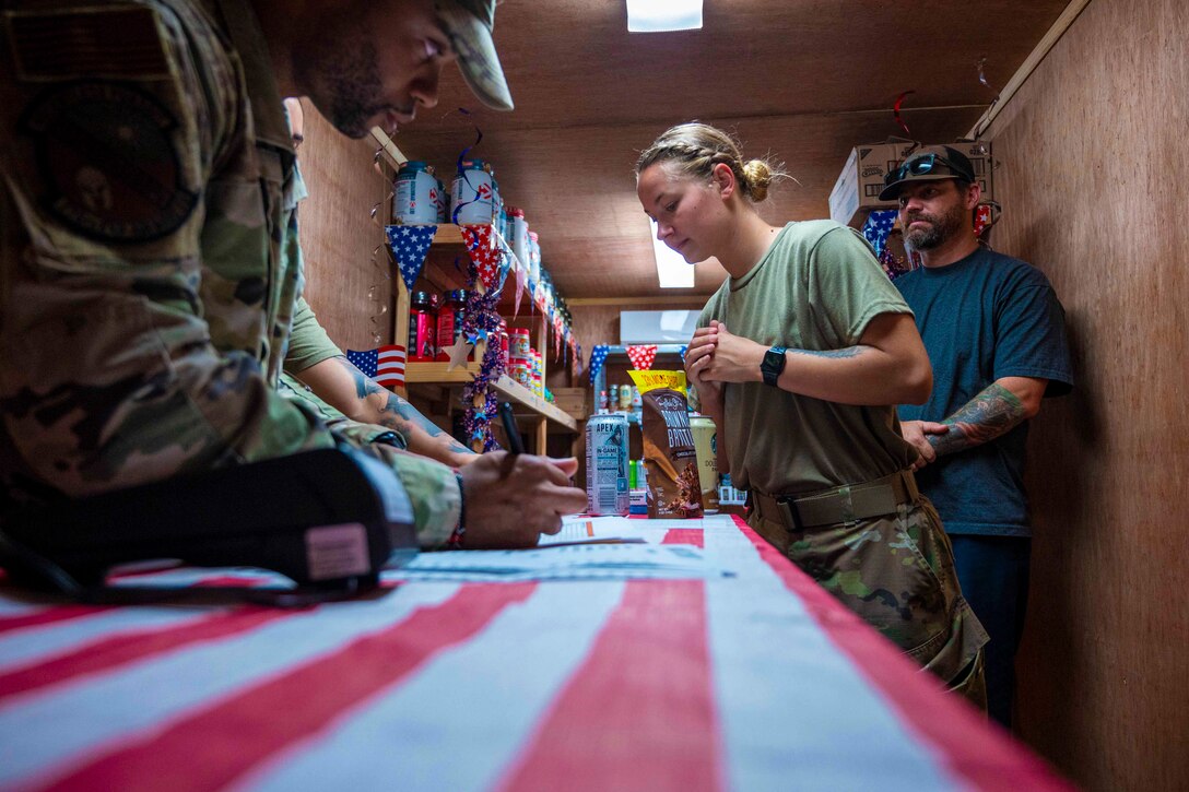 A service member stands behind a table as others stand on the other side looking at items.