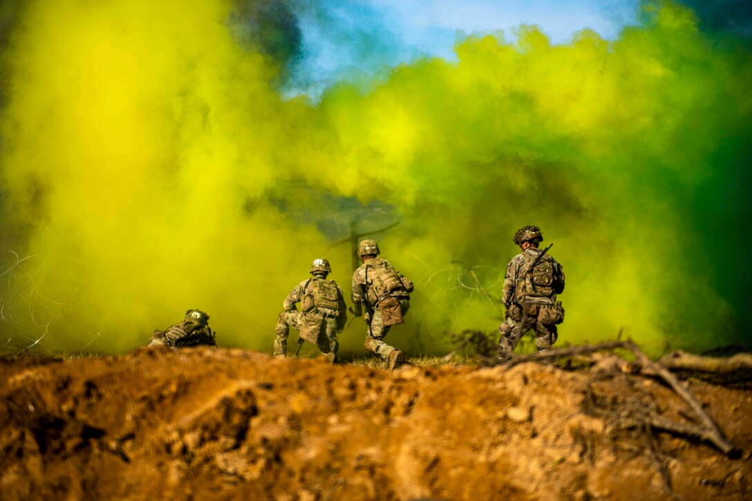 Soldiers place explosives on concertina wire under the cover of yellow and green smoke.