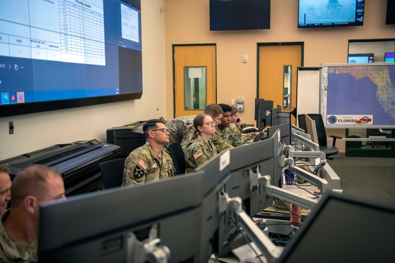 Soldiers sit behind a row of computer screens.