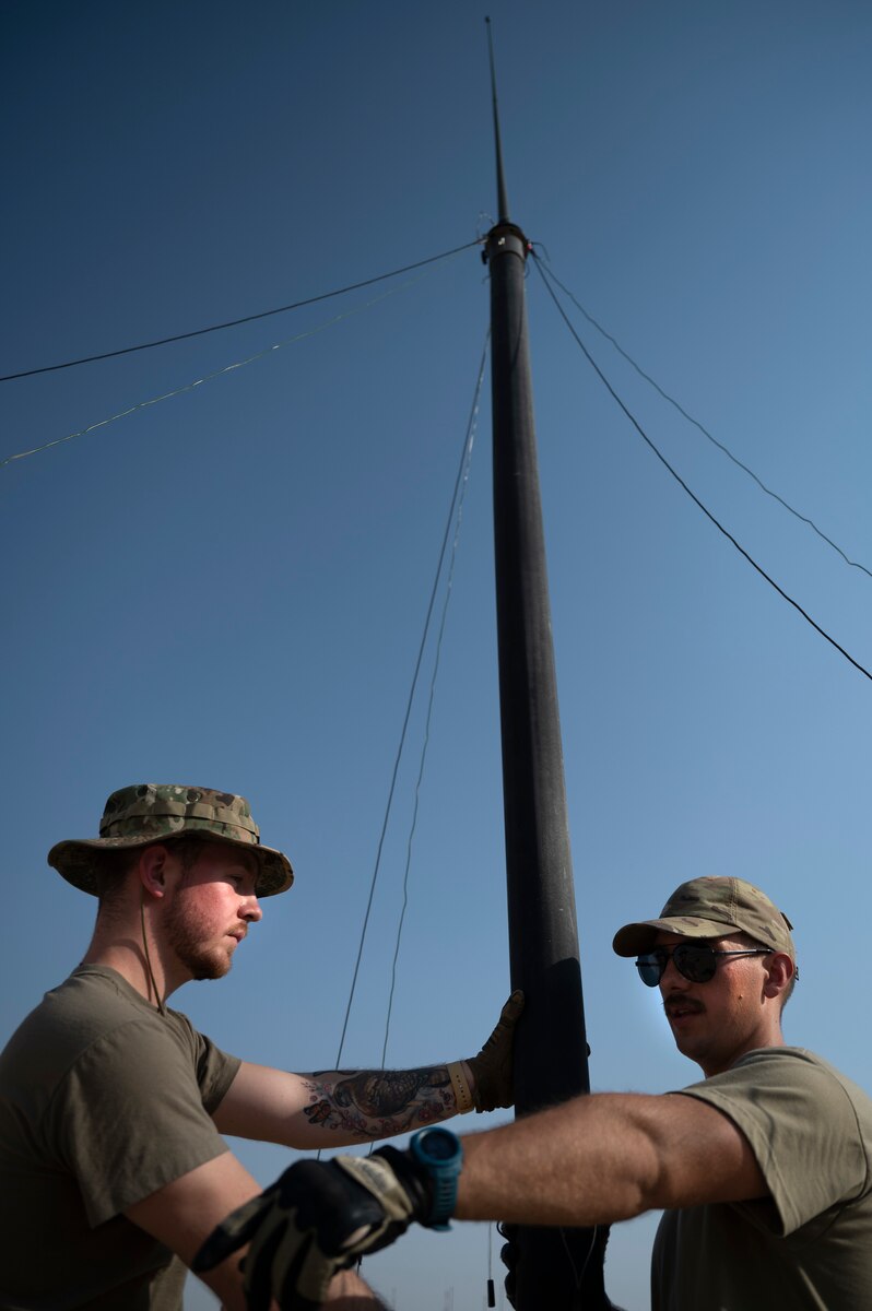U.S. Air Force Senior Airman Devin Blount, 386th Expeditionary Communications Squadron and Senior Airman Daniel Stricker, 386th ECS Radio Frequency transmission technician hold on to a mast communication system while Airmen set stakes to hold the system in place during Operation Agile Spartan III at an undisclosed location, September 12, 2022. The mast communications system is a portable communications system that a minimum of three Airmen can set up to strengthen communications quickly. (U.S. Air Force photo by Staff Sgt. Dalton Williams)