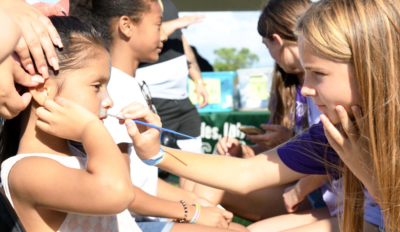 A youth member of the U.S. Naval Support Activity (NSA) Naples community gets her face painted by local students during the "Back 2 School" block party event, hosted by Morale, Welfare, and Recreation, onboard NSA Naples Support Site in Gricignano di Aversa, Italy, Aug. 19, 2022.