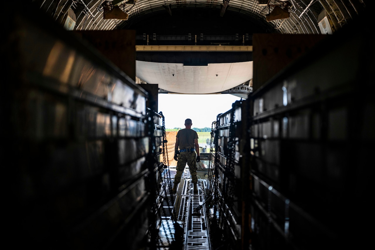An airman stands at the end of a row of containers.