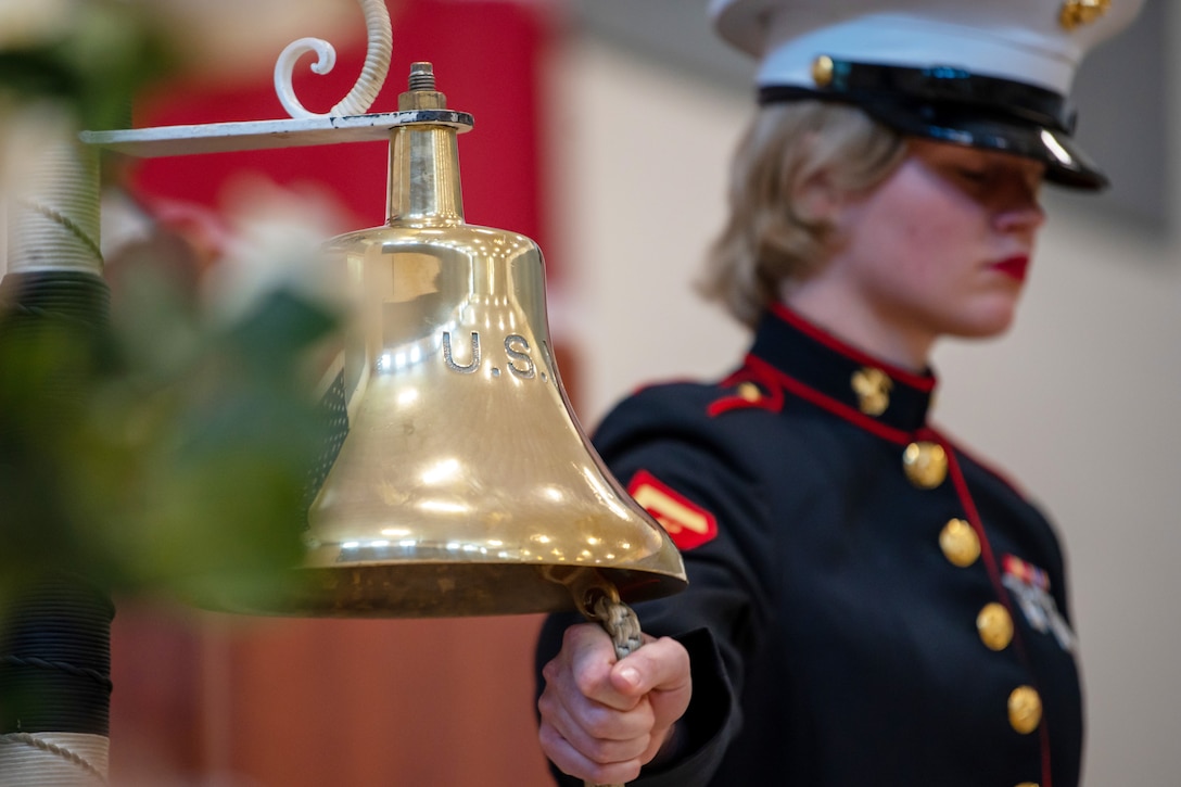 A service member in formal uniform prepares to ring a large bell.