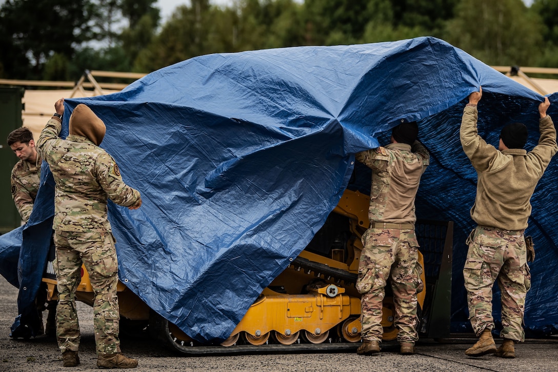 Four airmen place a tarp over equipment.