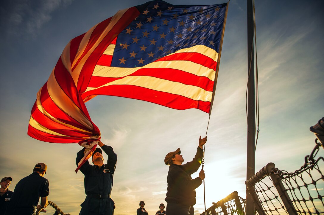 Two sailors lower the ensign.